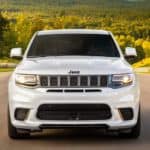 A white 2020 Jeep Grand Cherokee Trackhawk is shown from the front with trees in the distance.