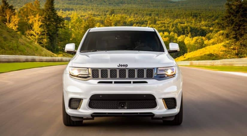 A white 2020 Jeep Grand Cherokee Trackhawk is shown from the front with trees in the distance.