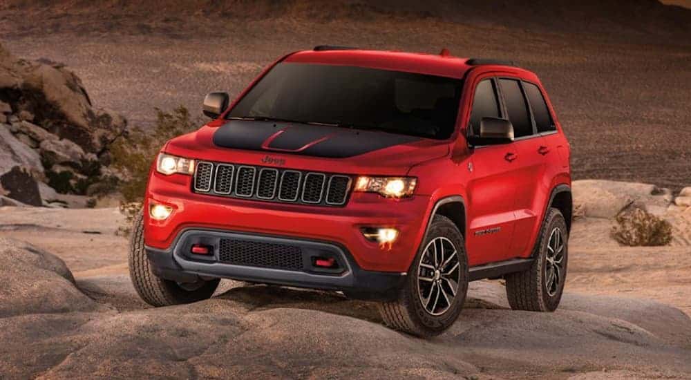 A red 2020 Jeep Grand Cherokee Trailhawk, which is a popular option at Jeep Dealerships, is parked on a large rock.