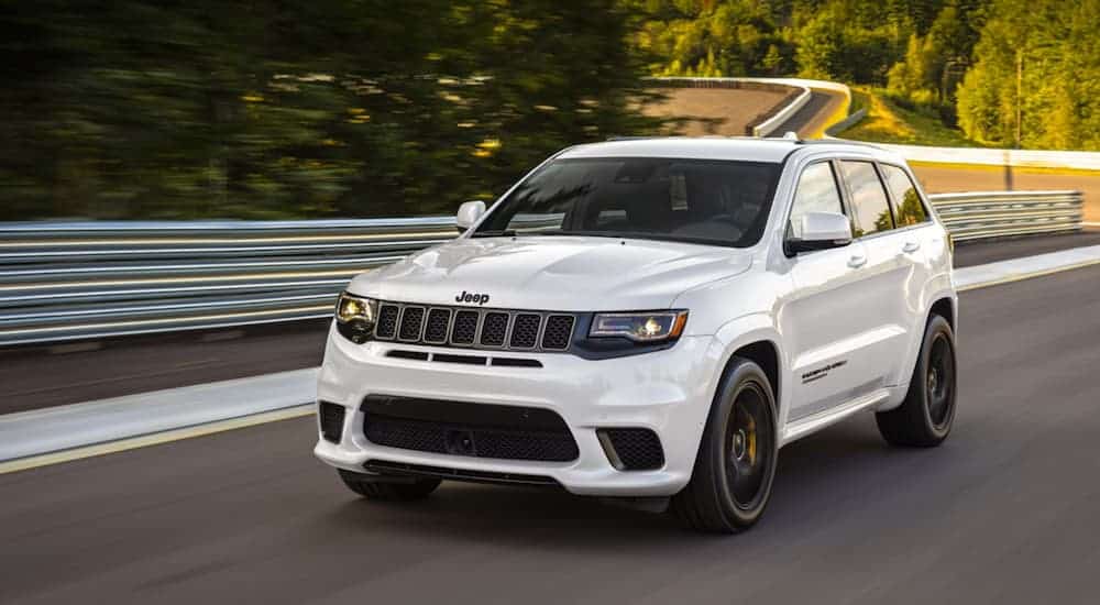 A white 2020 Jeep Grand Cherokee is driving on a tree-lined racetrack.