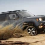 A grey 2020 Jeep Renegade is driving through the desert while kicking up sand.