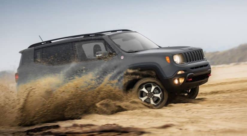 A grey 2020 Jeep Renegade is driving through the desert while kicking up sand.