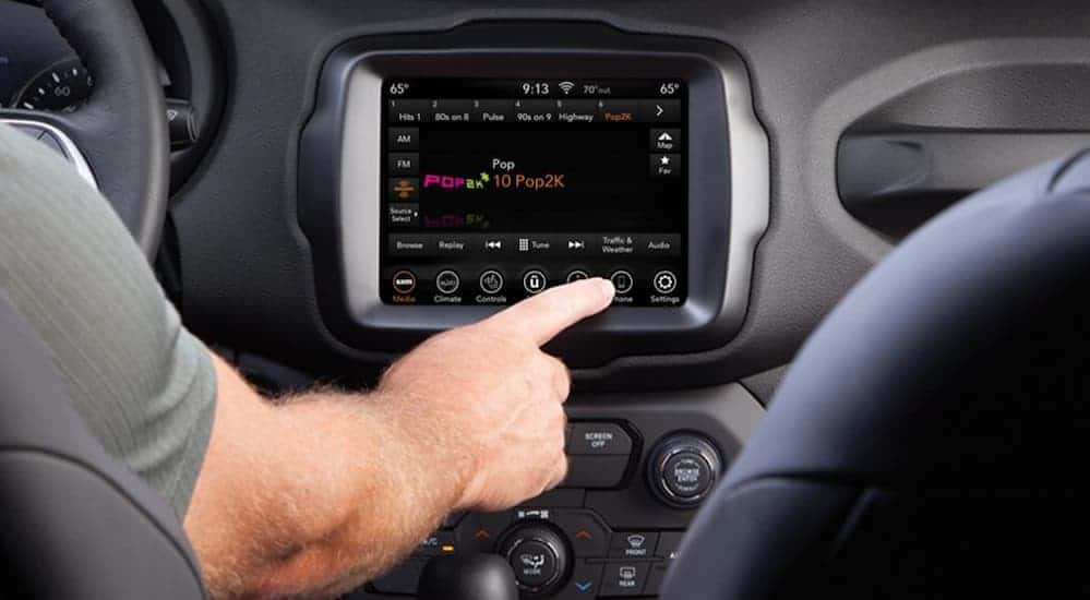 A hand is shown touching the infotinament screen of a 2020 Jeep Renegade.