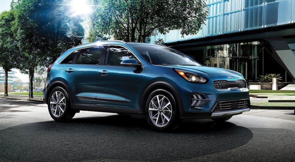 A blue 2020 Kia Niro is parked in front of a glass building.