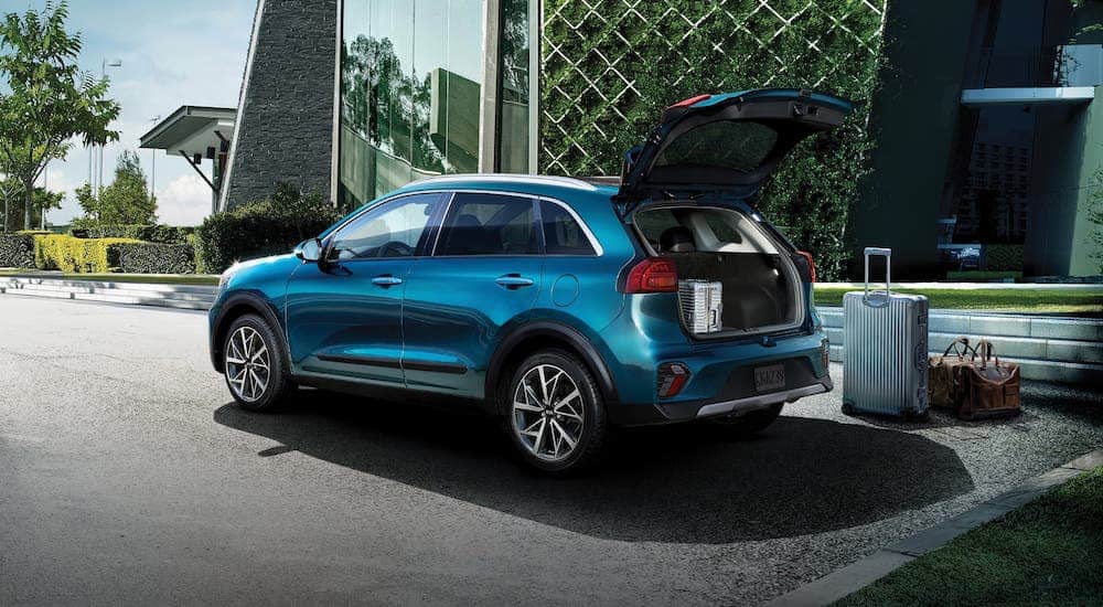 Luggage is sitting outside a blue 2020 Kia Niro that has the rear liftgate open.