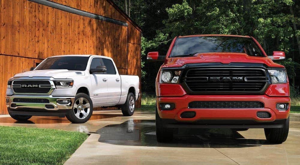 A red and a white 2020 Ram 1500s from the front in front of a barn