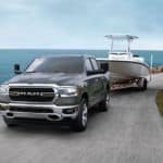 A gray 2020 Ram 1500 towing a boat next to a body of water