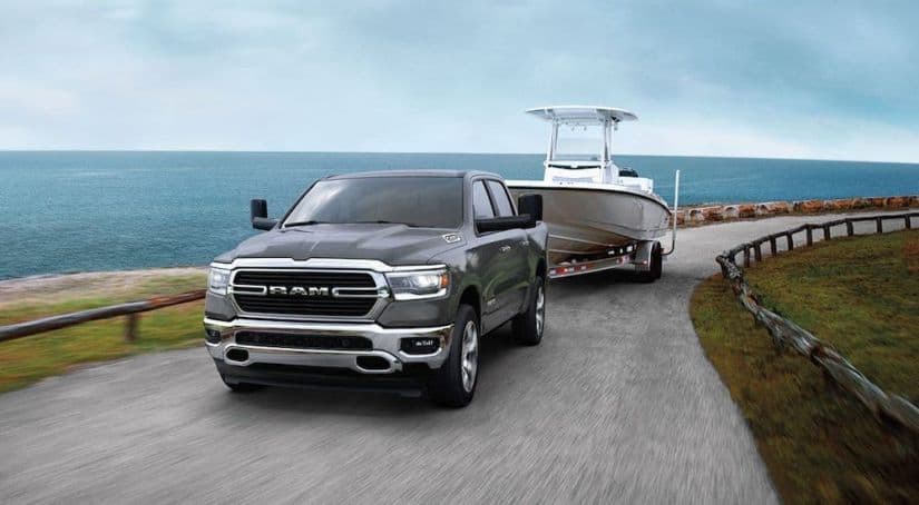 A gray 2020 Ram 1500 towing a boat next to a body of water