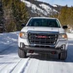 A white 2021 GMC Canyon AT4 is driving forward on a snow covered road.