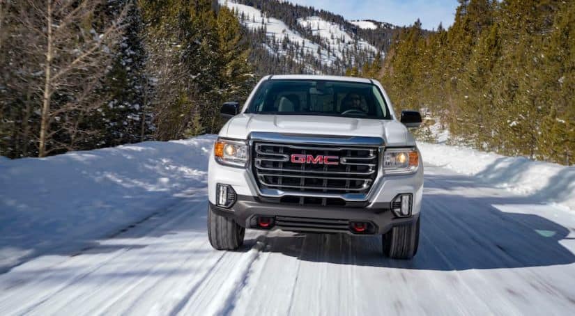 A white 2021 GMC Canyon AT4 is driving forward on a snow covered road.