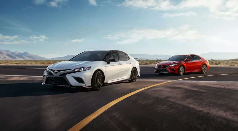 A red 2020 Toyota Camry is driving behind a white one on a racetrack.