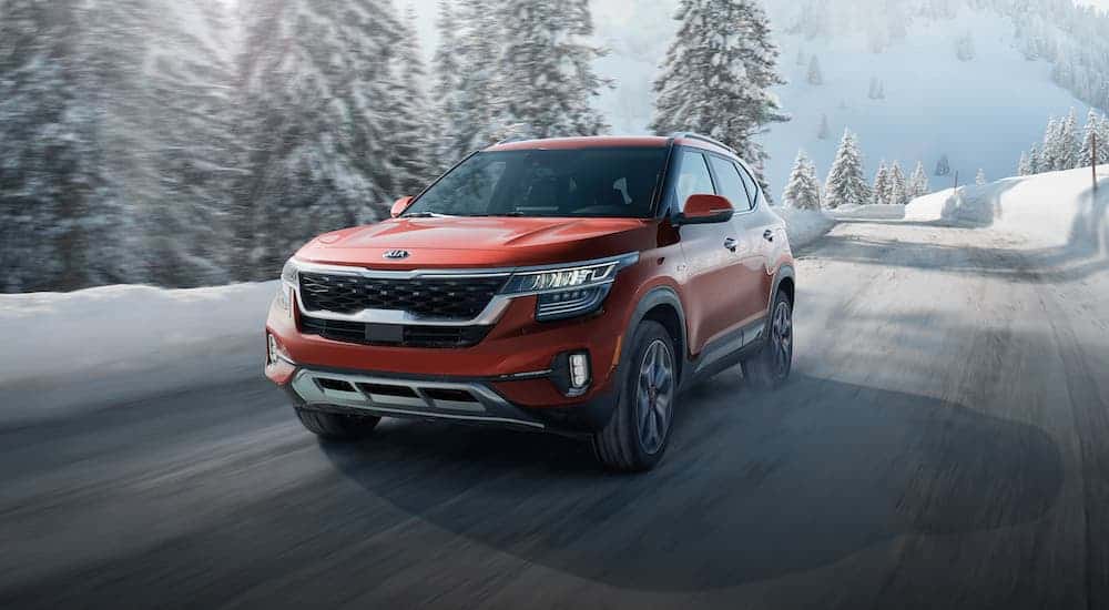 A red 2021 Kia Seltos driving on a snowy road with snow-covered mountains and trees in the distance
