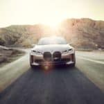A rose gold 2021 BMW i4 is driving in a desert, shown from the front.