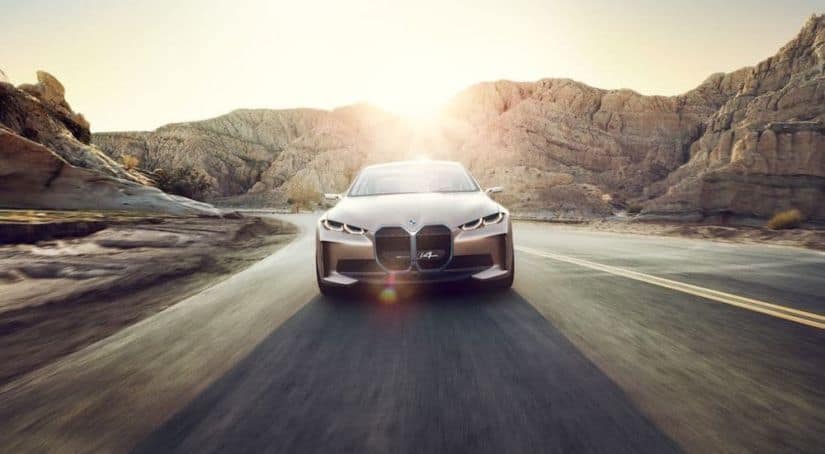 A rose gold 2021 BMW i4 is driving in a desert, shown from the front.