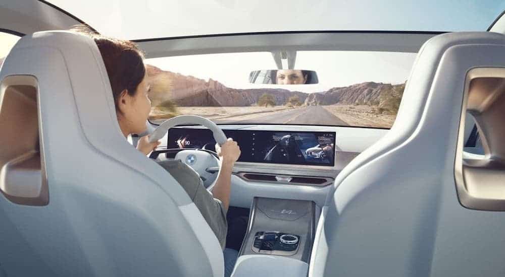 A woman is driving a 2021 BMW i4 on a desert road, shown from the rear seat.