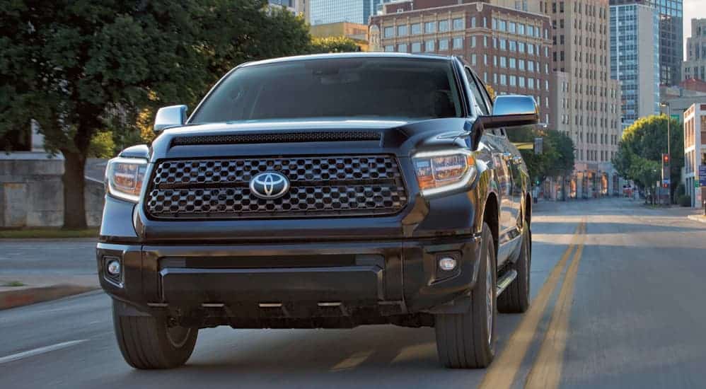 A black 2020 Toyota Tundra is driving on a city street with city buildings in the distance. 