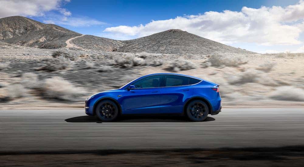 Constantly in current auto news, a blue Tesla Model Y is driving in a desert.