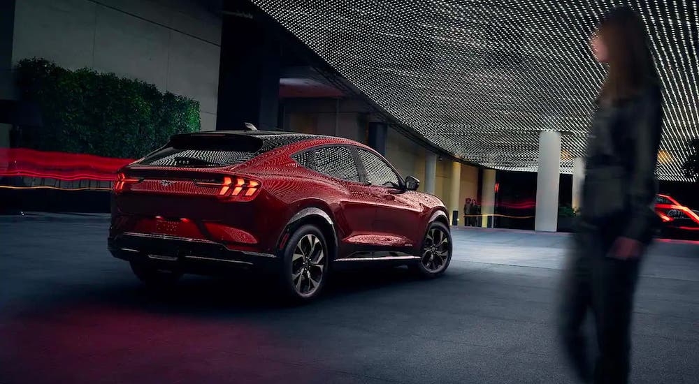 One of the new Ford SUVs, a red 2021 Ford Mustang Mach-E is parked under a lit overhang at night.