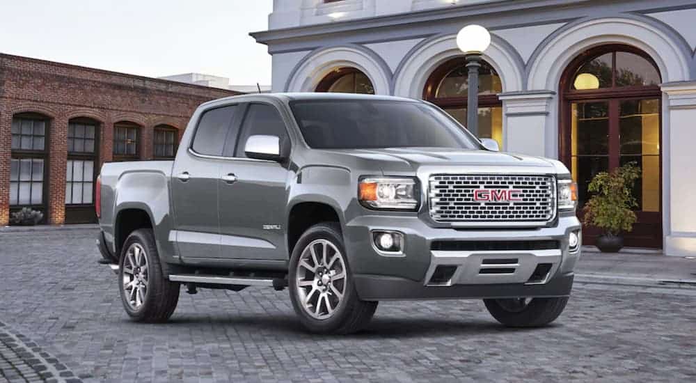 A silver 2020 GMC Canyon Denali, which is a popular option among GMC trucks, is parked in front of a white building. 