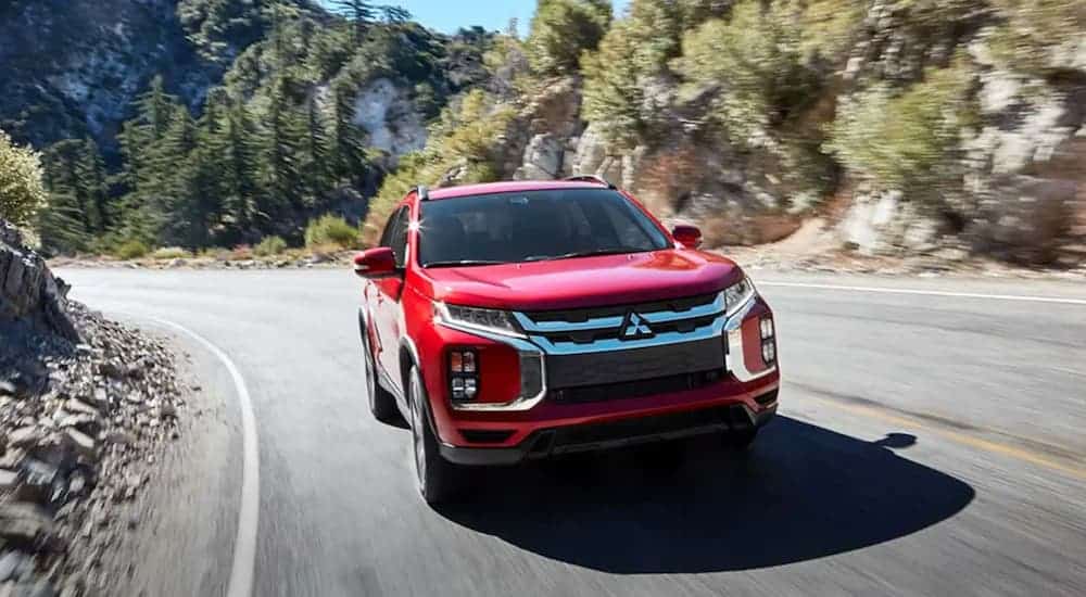 A red 2020 Mitsubishi Outlander Sport is driving around a corner in front of hills after leaving a Mitsubishi dealer.