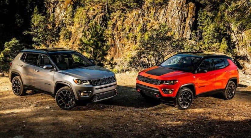 A silver 2018 Jeep Compass is parked next to an orange one in front of a rock wall.