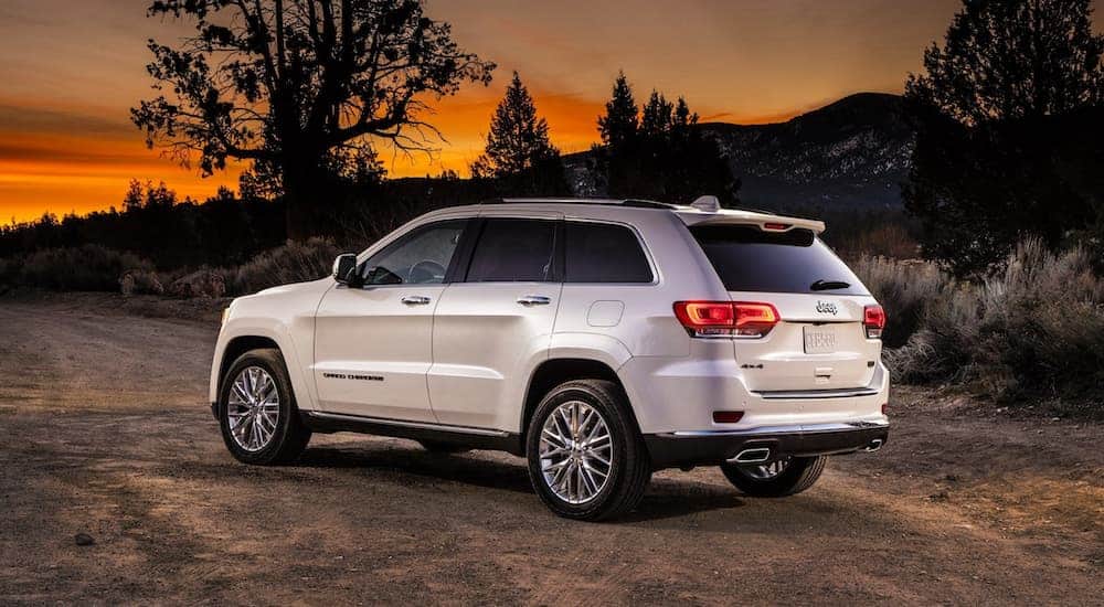 A white 2018 Jeep Grand Cherokee is parked on a dirt road at sunset.