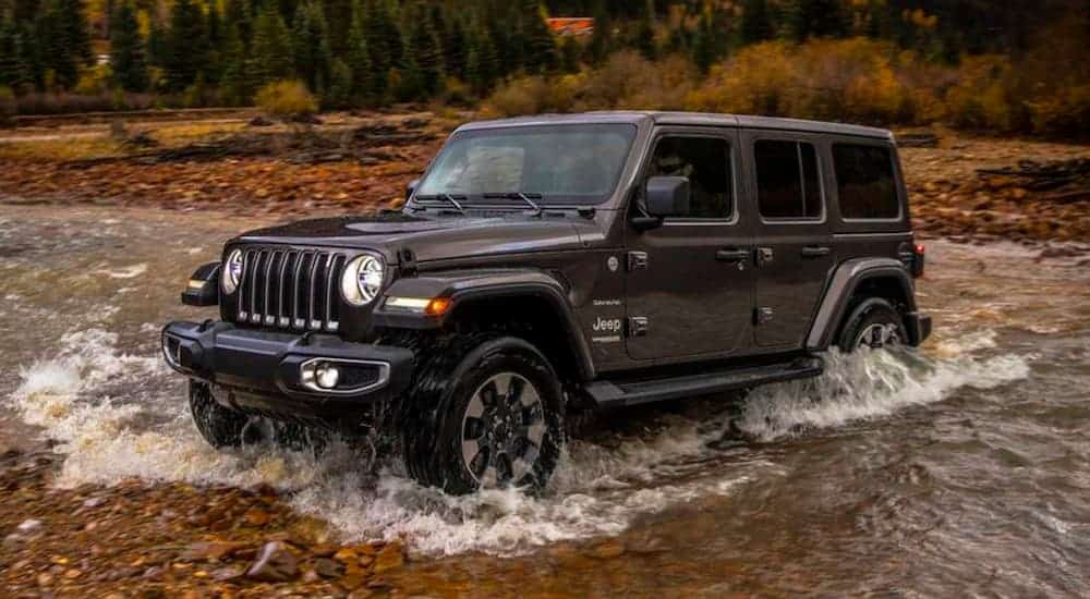A dark grey 2018 Jeep Wrangler is off-roading in a river after leaving a used car dealer.