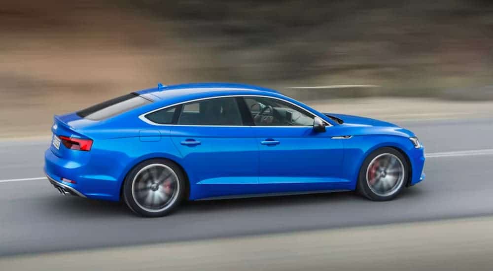 A blue 2017 Audi A5 is driving with a blurred background.
