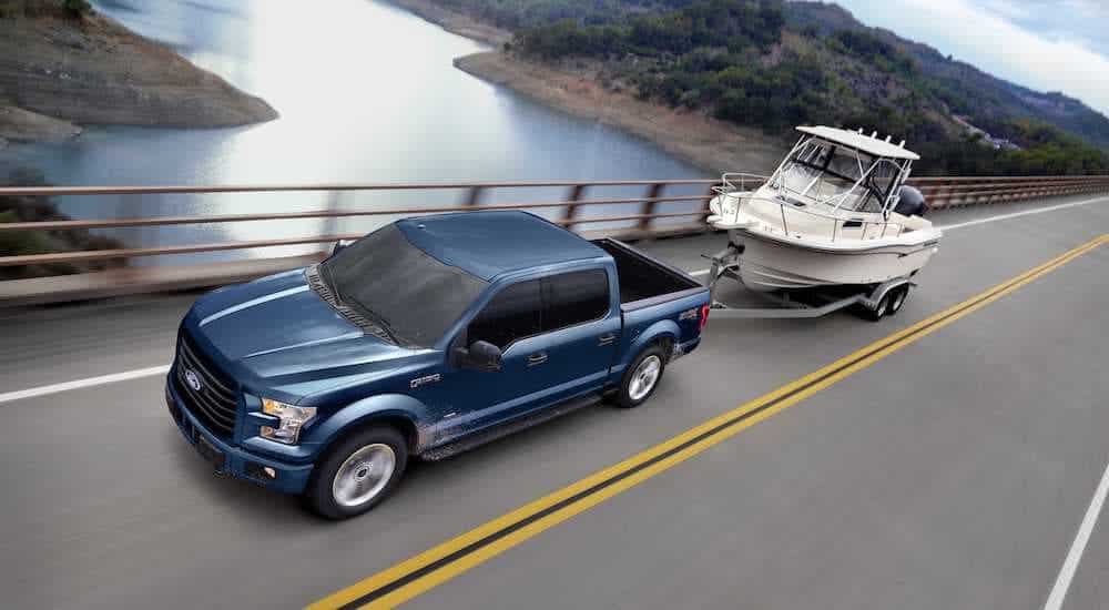 A blue 2017 Ford F-150 XLT is towing a boat over a bridge.
