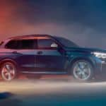 A blue 2020 BMW X5 is driving through an industrial area at night.