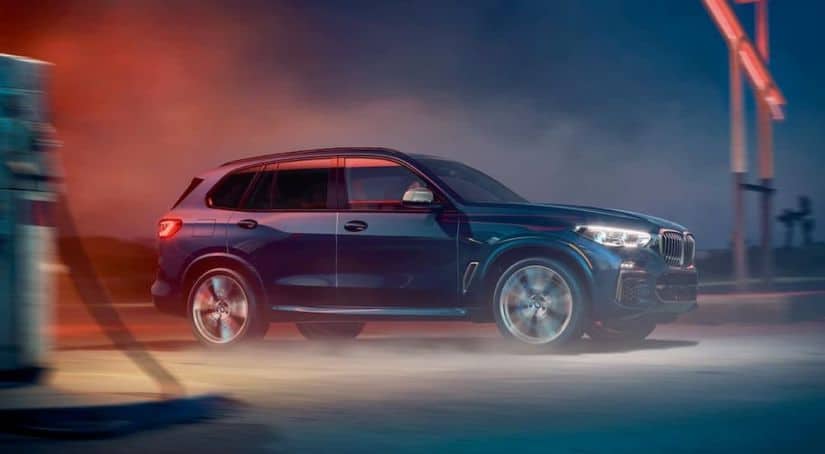 A blue 2020 BMW X5 is driving through an industrial area at night.