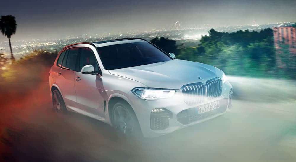 A silver 2020 BMW X5 is driving at night with a view of a lit up city.