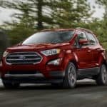A red 2020 Ford Ecosport is driving past pine trees.