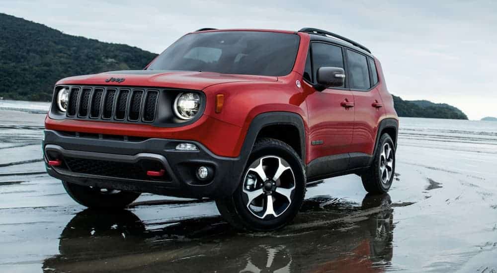A red 2020 Jeep Renegade is driving in the wet sand at the beach.