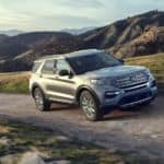 A silver 2020 Ford Explorer, which wins when comparing the 2020 Ford Explorer vs 2020 Mazda CX-9, is driving on a dirt road in front of mountains.