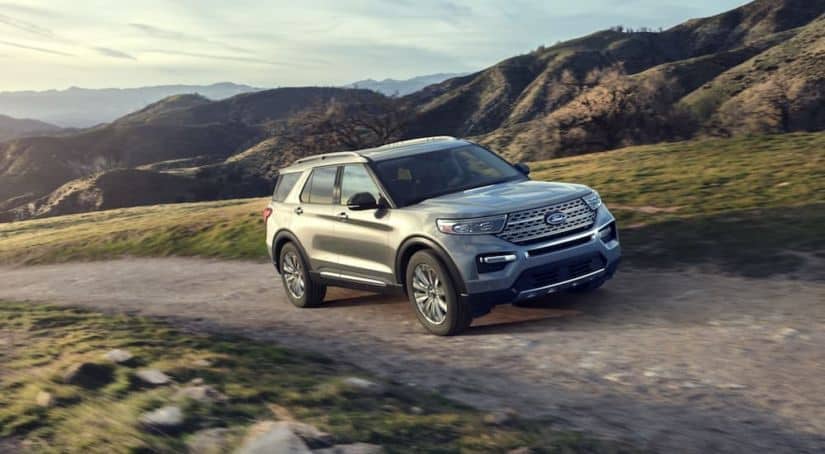 A silver 2020 Ford Explorer, which wins when comparing the 2020 Ford Explorer vs 2020 Mazda CX-9, is driving on a dirt road in front of mountains.