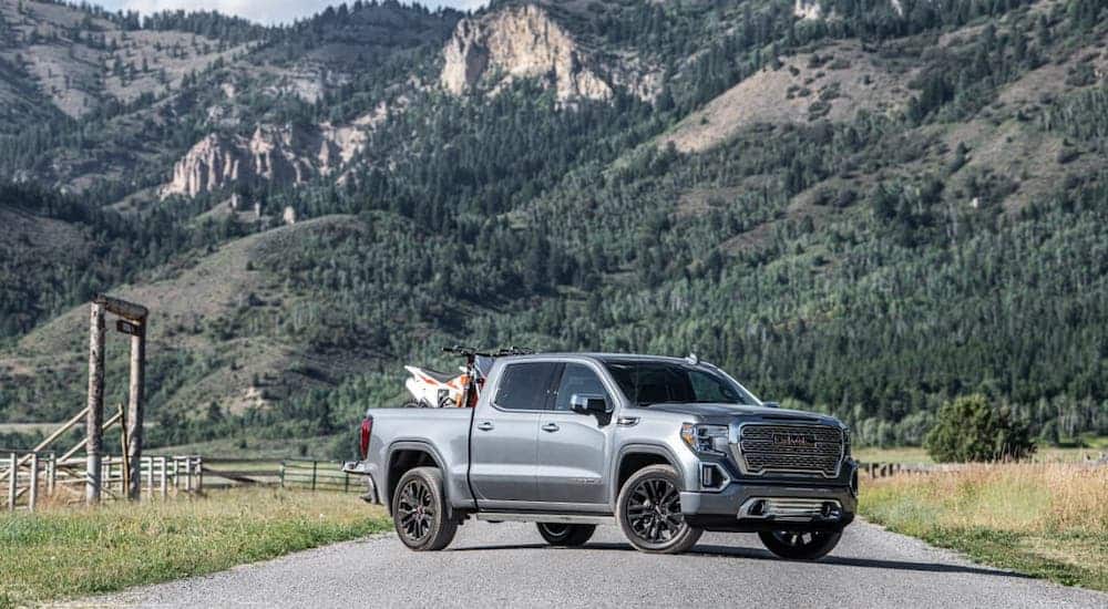 A silver 2020 GMC Sierra Denali is parked in front of mountains with a dirt bike in the bed.
