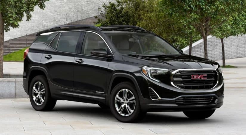 A black 2020 GMC Terrain, wich wins when comapring the 2020 GMC Terrain vs 2020 Nissan Rogue, is parked in front of city steps and trees.