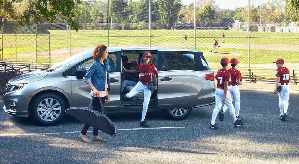 A children's baseball team is unloading from a silver 2020 Honda Odyssey LX.