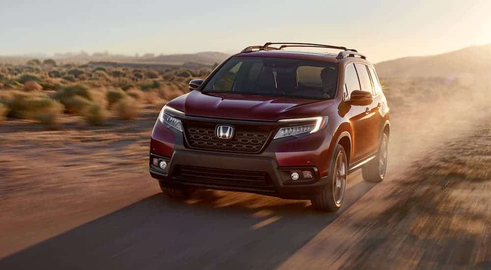 A red 2020 Honda Passport is driving on a dirt road in the desert.