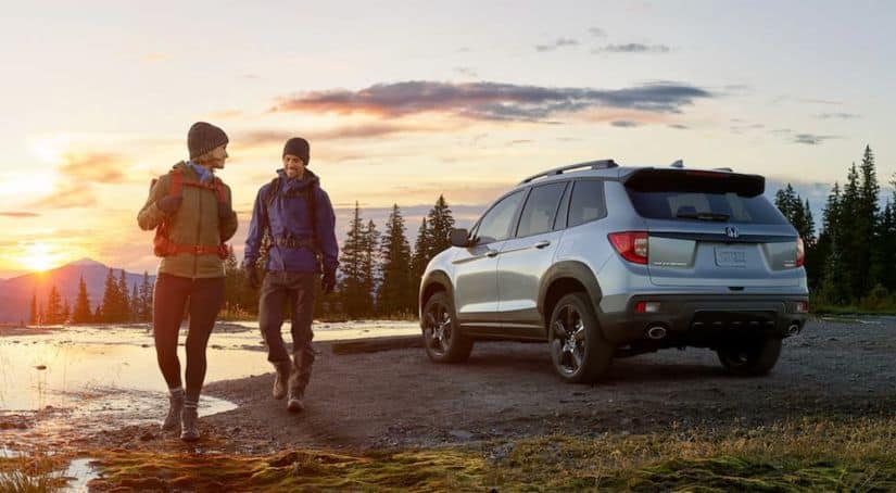 A couple is walking away from a silver 2020 Honda Passport for a sunrise hike.