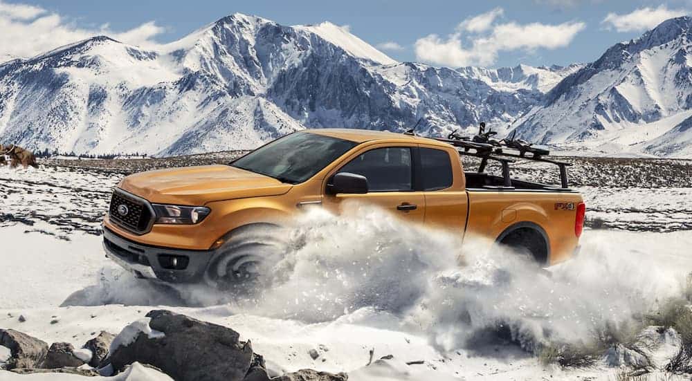 A gold 2020 Ford Ranger is off-roading in the snow in front of mountains.