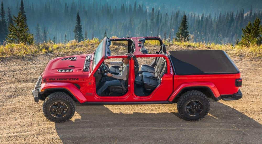 A red 2020 Jeep Gladiator is driving on a dirt road with the top and doors off.