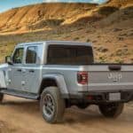 A silver 2020 Jeep Gladiator, which wins when comparing the 2020 Jeep Gladiator vs 2020 Ford Ranger, is driving on a dirt road in the desert.