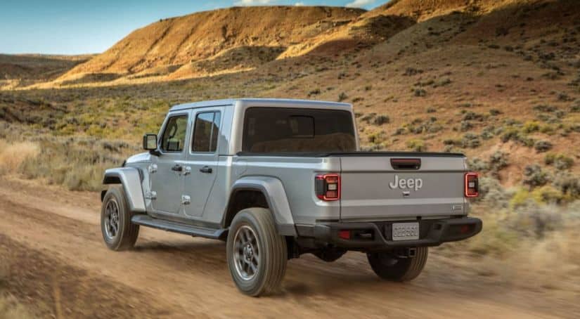A silver 2020 Jeep Gladiator, which wins when comparing the 2020 Jeep Gladiator vs 2020 Ford Ranger, is driving on a dirt road in the desert.