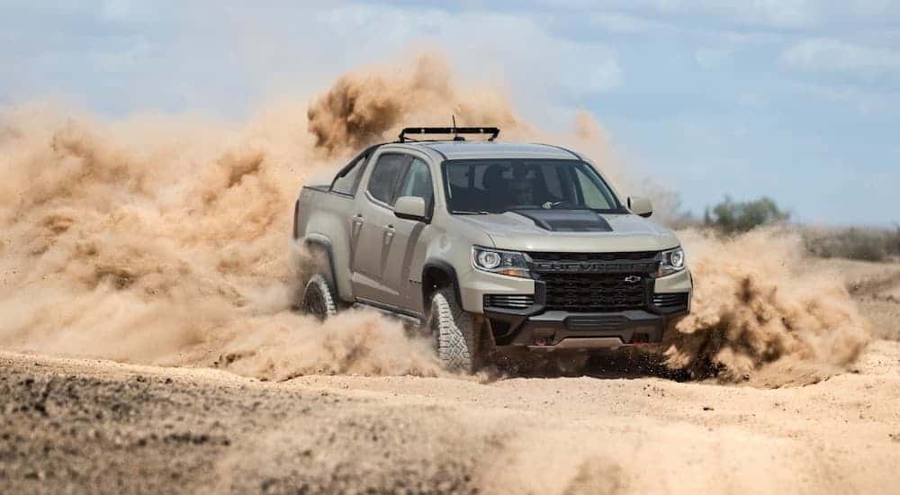 A tan 2021 Chevy Colorado ZR2 is racing in sand and kicking up a dust cloud.