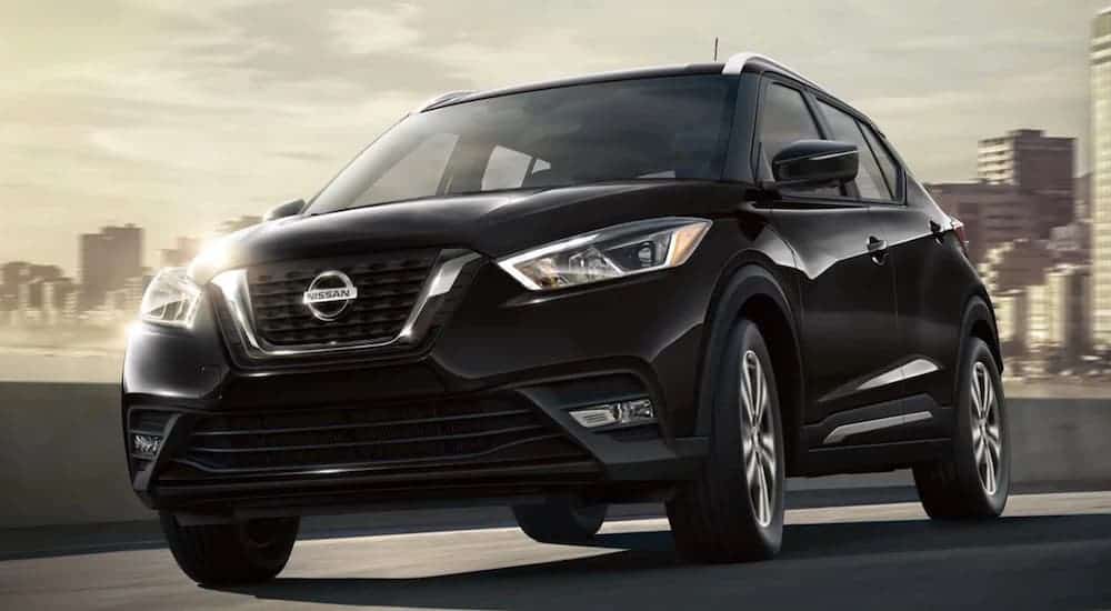 A black 2020 Nissan Kicks is driving away from a city with a cloudy sky.