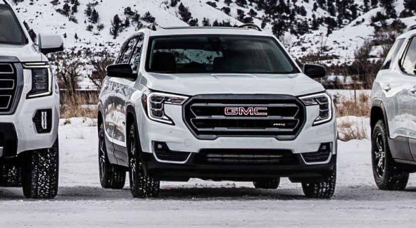 A white 2021 GMC Terrain AT4, which wins in comparing the 2021 GMC Terrain vs 2020 GMC Terrain, is parked in the snow between other 2021 GMC AT4 models.