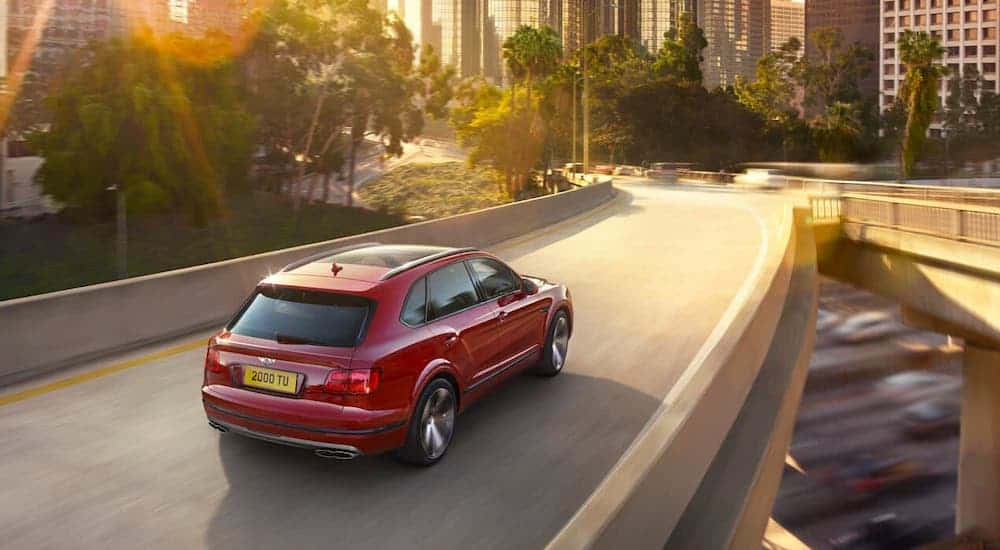 A red Bentley Bentayaga V8 is driving away on a bridge at sunset.