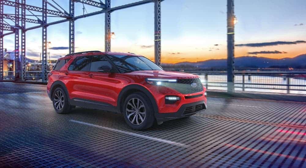 A red 2020 Ford Explorer ST is driving over a bridge at sunset.